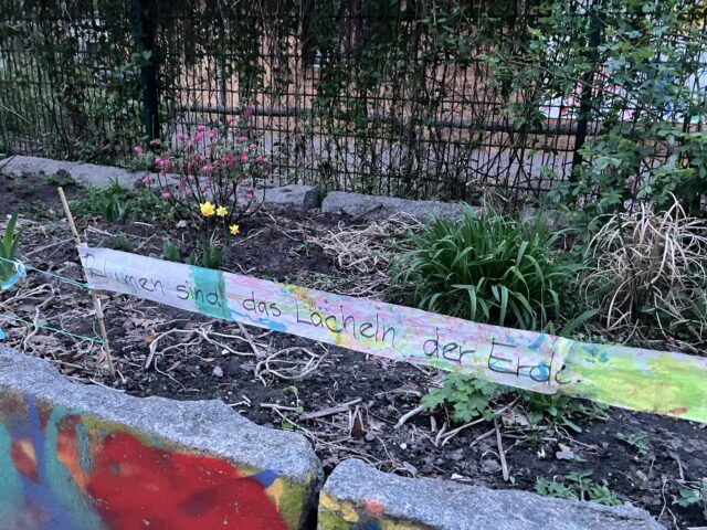 Ein Banner mit dem Text „Blumen sind das Lächeln der Erde“ auf den frisch bepflanzten Hochbeeten vor dem Spielhaus in der Sesenheimer Straße.