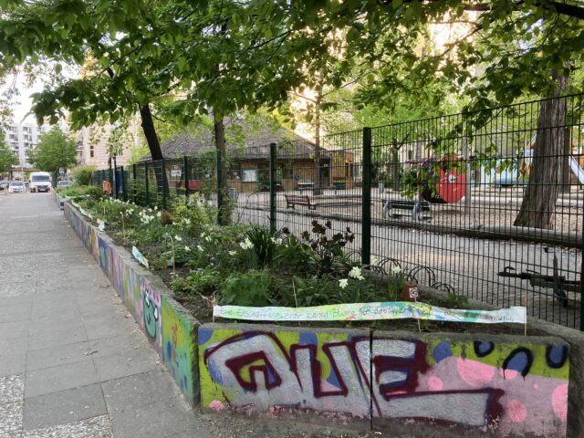 Ein handgemachtes Banner mit dem Text „Die Erschaffung einer kleinen Blume ist das Werk von Jahrtausenden (W. Blake)“ auf den frisch bepflanzten Hochbeeten vor dem Spielhaus, Sesenheimer Straße.