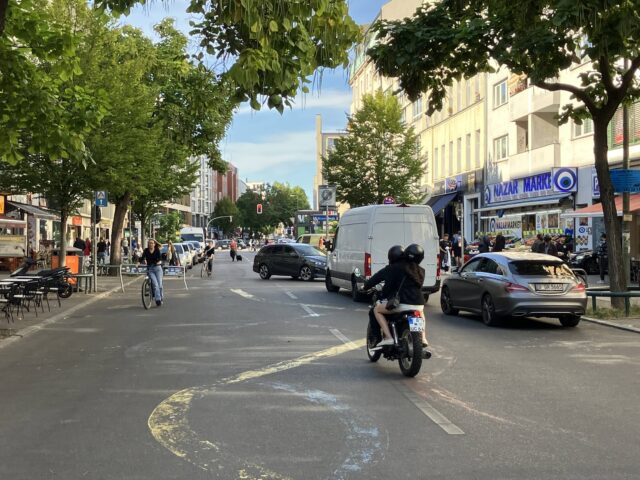 Ein Motorrad fährt durch die Fußgängerzone, in der auch einige Falschparker stehen.